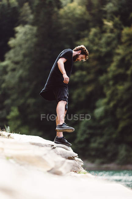 Человек, стоящий на каменном краю над рекой на природе — стоковое фото