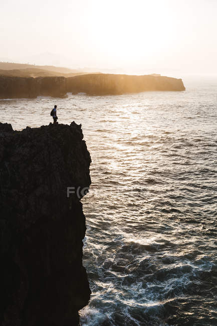 Vista lejana de la silueta de la persona de pie en el acantilado sobre el mar - foto de stock