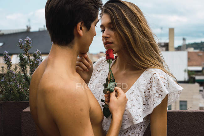 Retrato de un hombre sensual abrazando a una chica y tocándose la cara con rosa - foto de stock