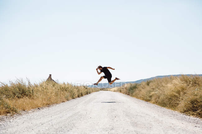 Вид сбоку на человека, позирующего в прыжке через сельскую дорогу — стоковое фото