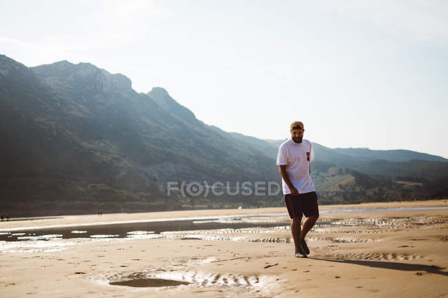 Vista frontal del hombre caminando en la playa sobre la costa plomada en el fondo - foto de stock
