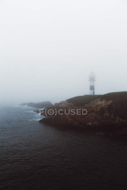 Landschaft aus nebligem Leuchtturm an der felsigen Küste — Stockfoto
