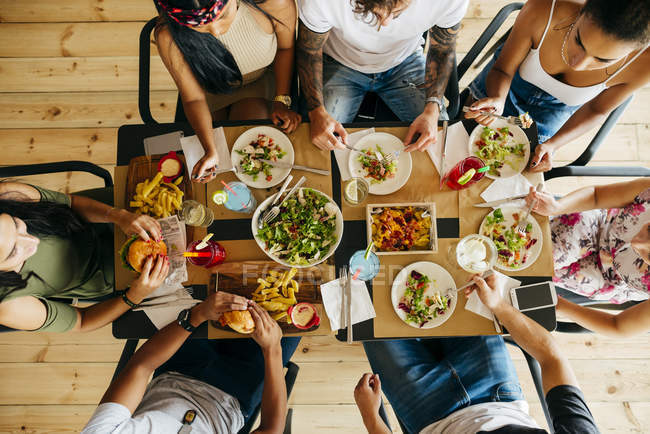 From above group of friends sitting together in restaurant and eating — Stock Photo