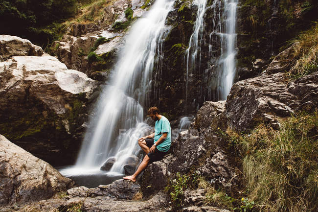 Вид сбоку на человека, позирующего на скалах у водопада — стоковое фото