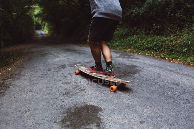 Crop man on skateboard riding on forest road — Stock Photo