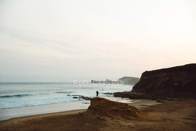 Vista distante dell'uomo che posa sulla scogliera costiera contro il paesaggio marino — Foto stock