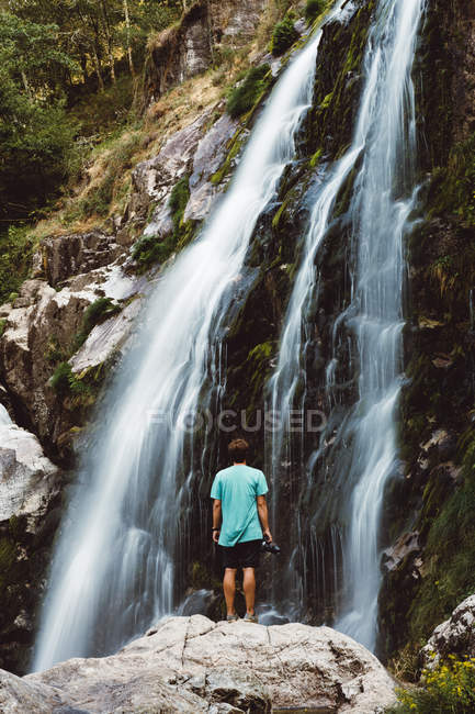 Visão traseira do homem em pé no penhasco e olhando para a cachoeira — Fotografia de Stock