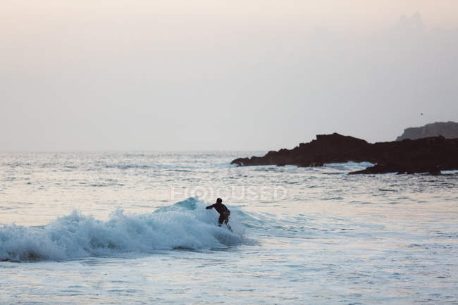 Vista lateral do surfista montando na onda na luz do pôr do sol — Fotografia de Stock
