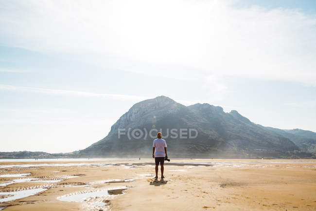 Rückansicht eines Mannes, der am sandigen Ufer mit Klippen steht — Stockfoto