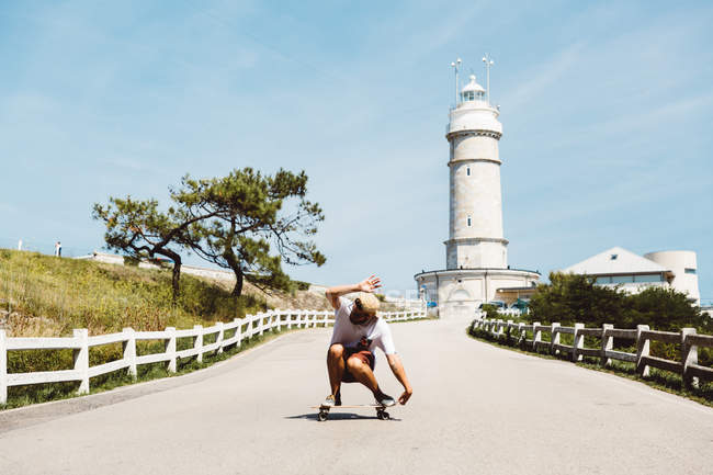 Seitenansicht des Mannes Skateboarding in Gasse führt zu Leuchtturm — Stockfoto