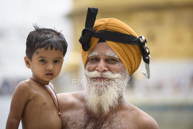 Sorridente anziano adulto barbuto uomo tenendo ragazzo indiano su mani. — Foto stock