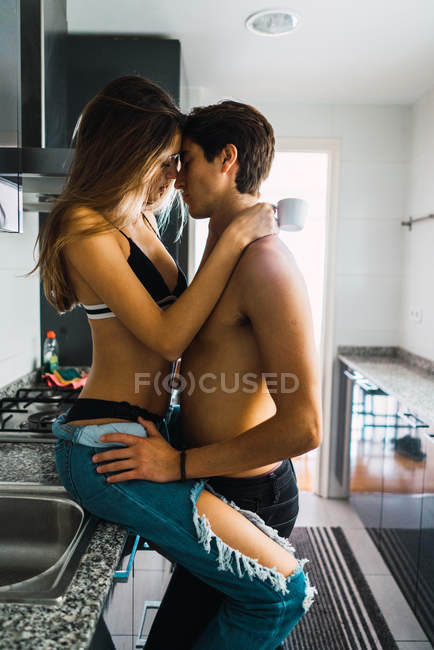 Vista lateral do casal abraçando no balcão da cozinha em casa — Fotografia de Stock