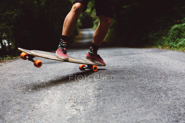Crop man on skateboard on tricking on asphalt road — Stock Photo