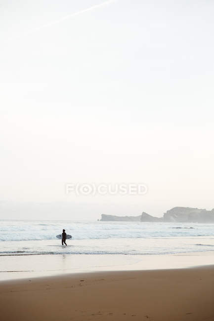 Surfista caminhando em ondas na praia à beira-mar — Fotografia de Stock