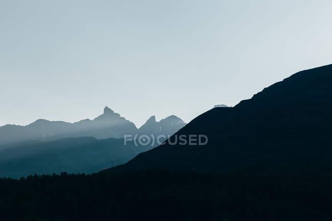 Vista para altos picos silhuetas sobre o céu nebuloso — Fotografia de Stock
