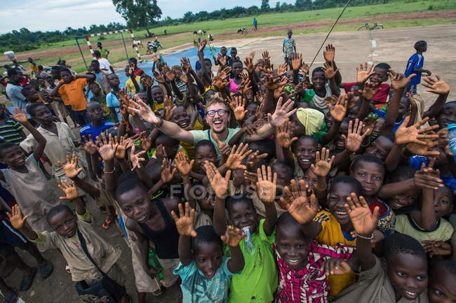 BENIN, ÁFRICA - 31 de agosto de 2017: Hombre posando entre niños africanos alegres con las manos en alto - foto de stock