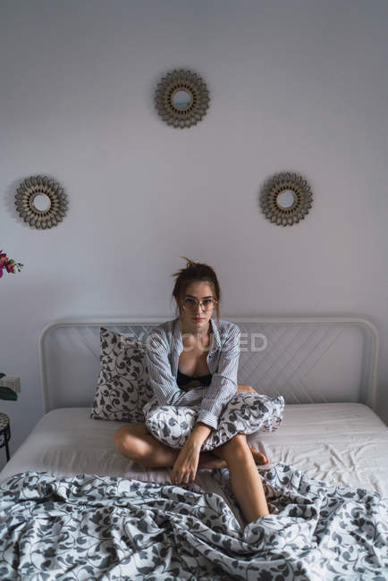Menina em óculos elegantes posando na cama e olhando para a câmera — Fotografia de Stock