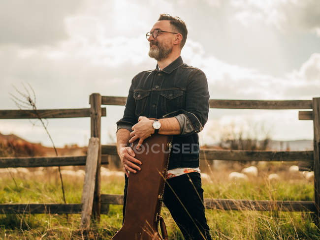 Side view of man posing with guitar case at countryside — Stock Photo
