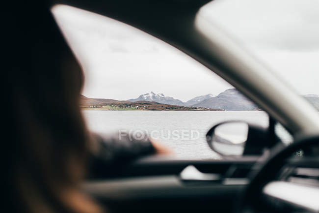Persona irreconocible conduciendo coche cerca del lago de las montañas en día nublado
. - foto de stock