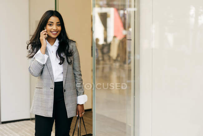 Elegant woman wearing jacket talking phone beside shop window — Stock Photo