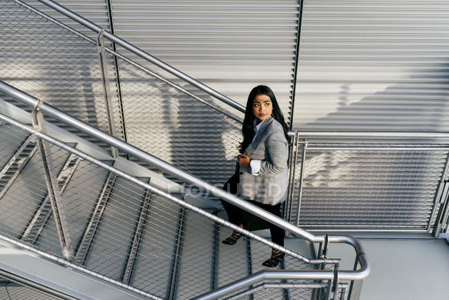 Vista de ángulo alto de la elegante mujer de negocios subiendo escaleras y mirando hacia otro lado - foto de stock