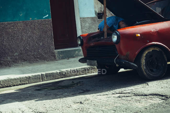 CUBA - AUGUST 27, 2016: Tilt view of man bending and repairing engine in old car at street. — Stock Photo