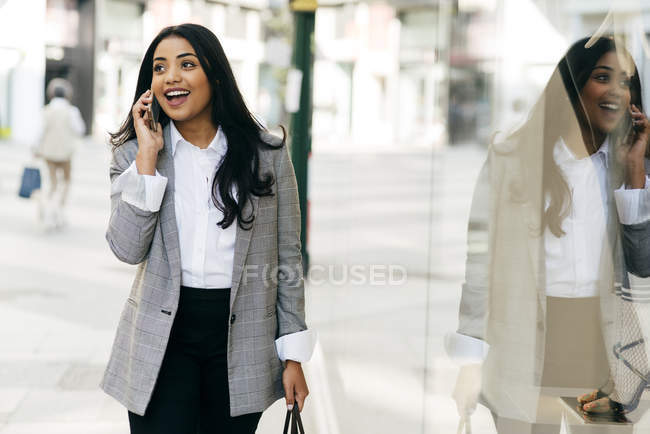 Portrait of elegant woman talking on phone and walking along shop windows — Stock Photo
