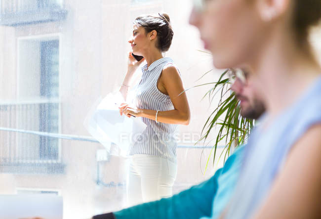 Vue latérale de femme d'affaires parlant sur smartphone dans un bureau moderne
. — Photo de stock