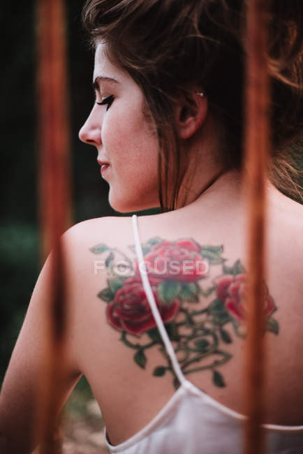 Vista posterior de la joven sensual mujer con tatuaje floral en la espalda mirando hacia abajo . - foto de stock