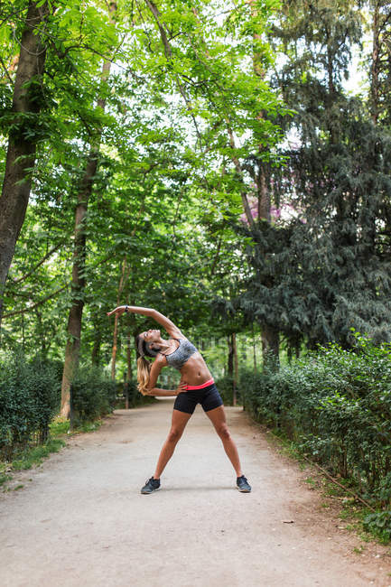Sporty girl performing yoga asana at park alley on sunny summer day — Stock Photo