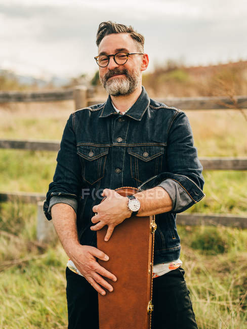 Дорослий чоловік з гітарною гітарою позує на сільській місцевості і дивиться на камеру — стокове фото