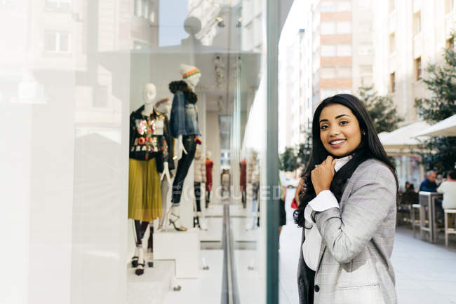 Retrato de una mujer sonriente con chaqueta posando cerca del escaparate - foto de stock