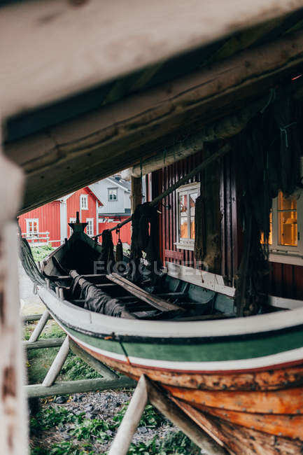 Old fishing boat with fishing nets standing under roof beside red house — Stock Photo