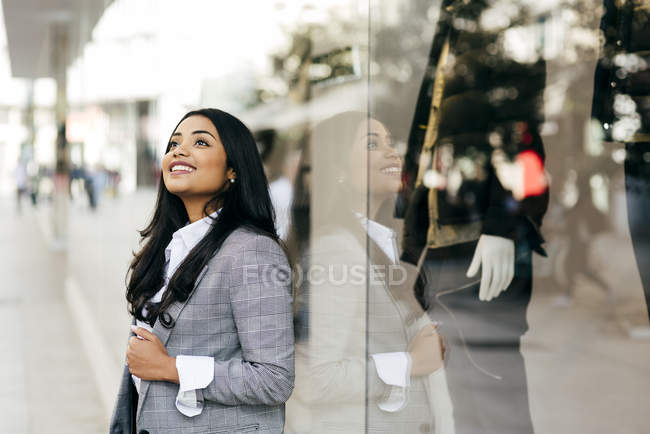 Mujer sonriente con chaqueta elegante posando cerca del escaparate - foto de stock