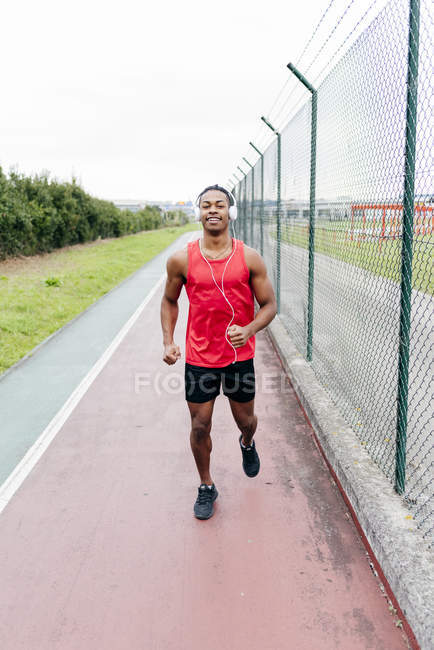 Front view of man wearing headphones running on track along fence — Stock Photo