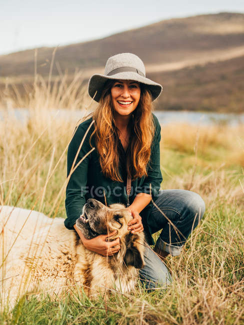 Retrato de mujer sonriente palmando perro en el campo - foto de stock