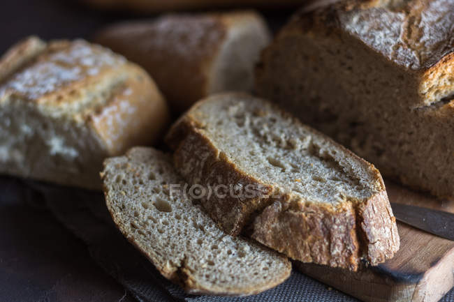 Close up view of home-made bread slices on rustic board with knifeac — Stock Photo
