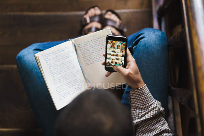 Overhead view of man holding notebook and using smartphone — Stock Photo