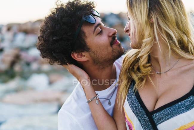 Embracing couple looking at each one over coastal rocks on backdrop — Stock Photo