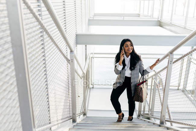 Элегантная деловая женщина разговаривает со смартфоном и поднимается по лестнице — стоковое фото