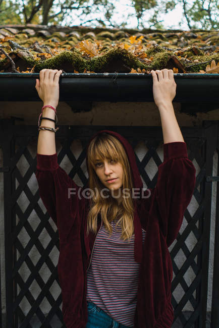 Casual brunette girl in red hoodie holding drain of arbor and looking at camera — Stock Photo