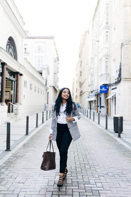 Elegante donna d'affari sorridente con borsa che cammina per strada e distoglie lo sguardo . — Foto stock