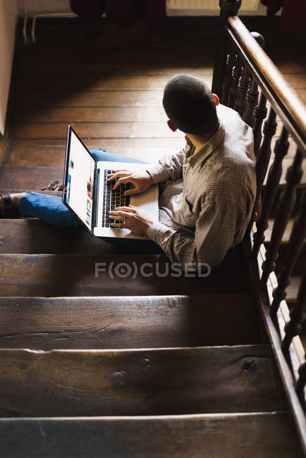 Vue à angle bas de l'étudiant avec ordinateur portable assis sur l'escalier — Photo de stock