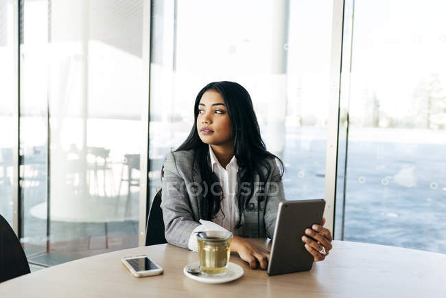 Portrait of elegant businesswoman sitting at table with tablet in hands and looking away — Stock Photo