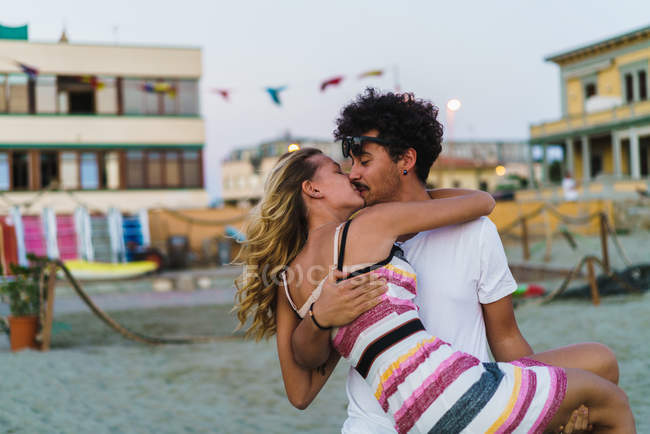 Ritratto di uomo che tiene fidanzata su mani e bacia in spiaggia — Foto stock