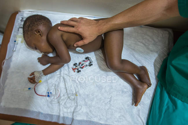 BENIN, AFRICA - AUGUST 30, 2017: Crop medic touching infant black boy in hospital. — Stock Photo