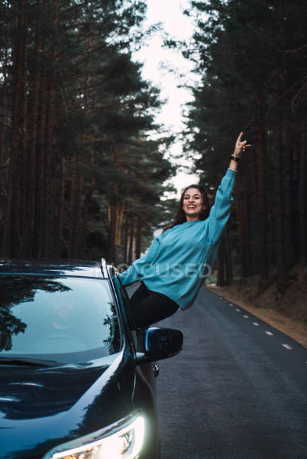 Smiling girl in blue sweatshirt leaning out of car window — Stock Photo