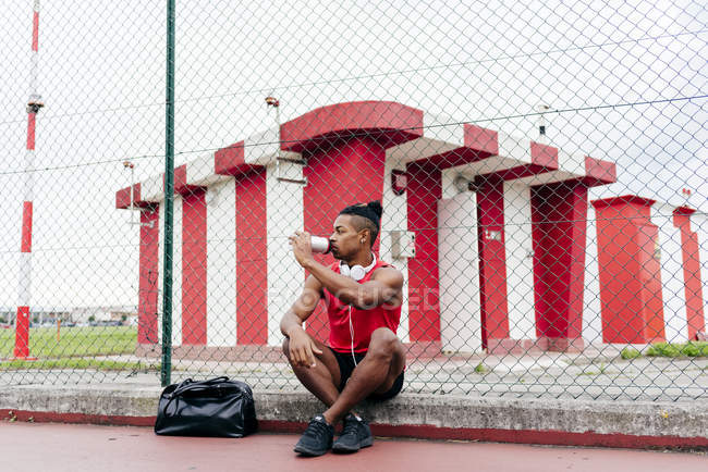 Sportler sitzt nach dem Training auf Spielplatz, trinkt Wasser und schaut weg — Stockfoto