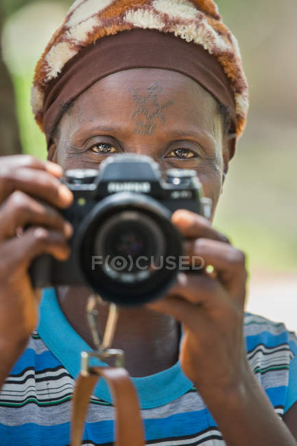 BENIN, AFRICA - AUGUST 31, 2017: Portrait of ethnic woman standing and taking shot with professional photo camera. — Stock Photo