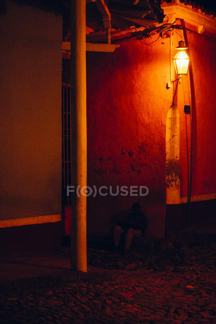 КУБА - 27 августа 2016 года: Человек, сидящий без земли в красном свете лампы, горящей на углу каменного здания — стоковое фото